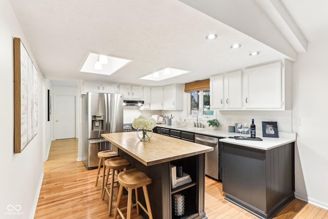 kitchen with a breakfast bar, white cabinetry, a skylight, stainless steel appliances, and a center island