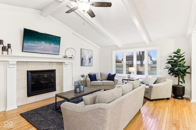 living room with lofted ceiling with beams, ceiling fan, a tiled fireplace, and hardwood / wood-style floors