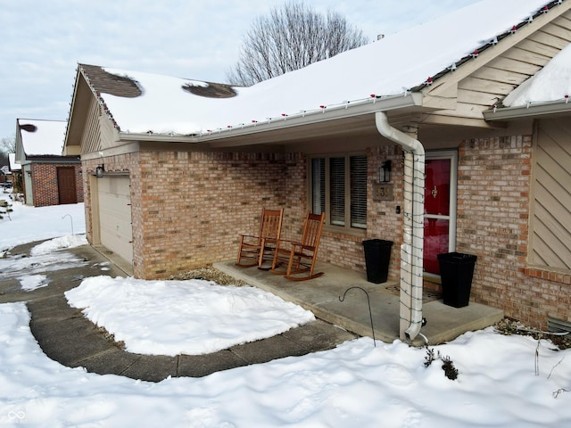 snow covered rear of property with covered porch and a garage