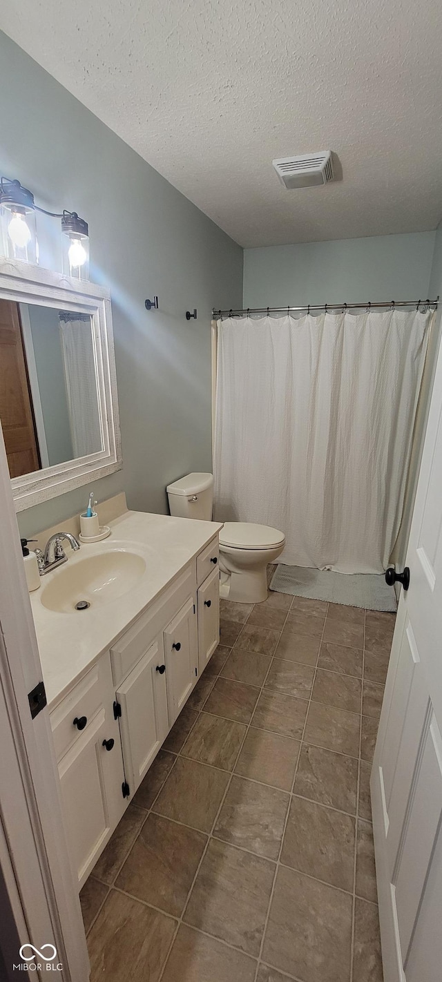 bathroom with a textured ceiling, vanity, and toilet