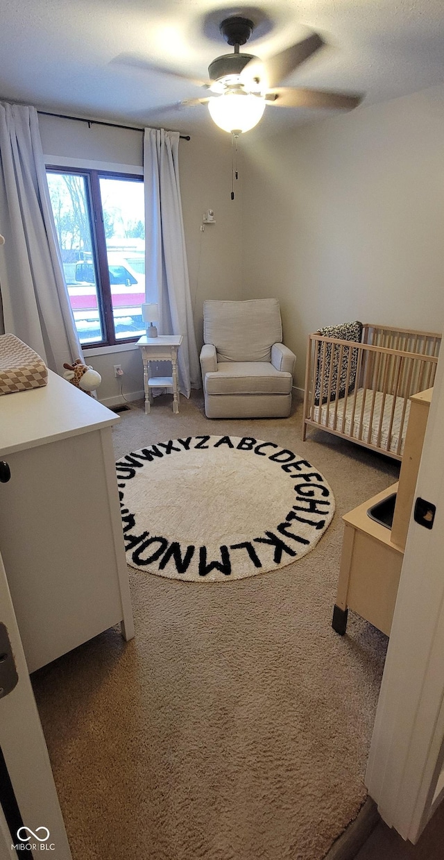 carpeted bedroom with ceiling fan and a crib