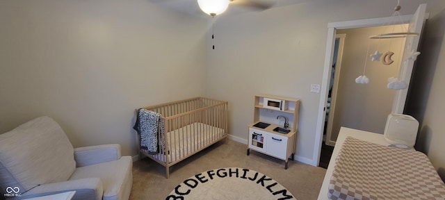 carpeted bedroom featuring ceiling fan and a nursery area