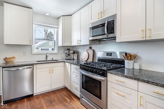 kitchen featuring appliances with stainless steel finishes, white cabinets, dark stone countertops, and sink