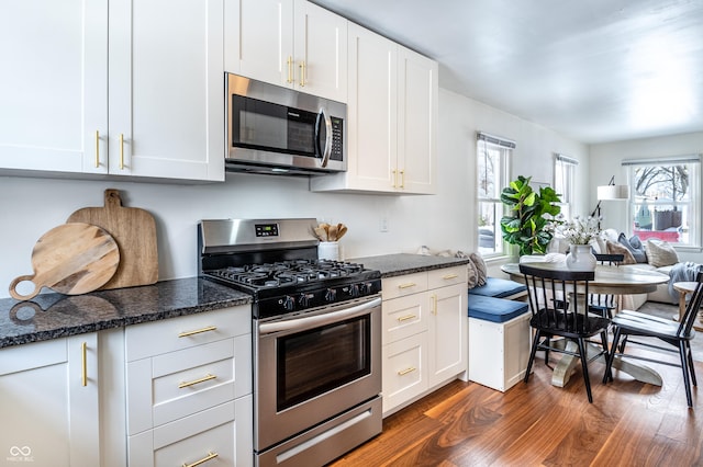 kitchen with stainless steel appliances, white cabinets, dark stone countertops, and dark wood-type flooring