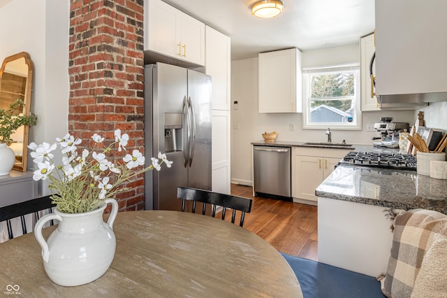 kitchen with dark stone countertops, stainless steel appliances, dark wood-type flooring, white cabinets, and sink