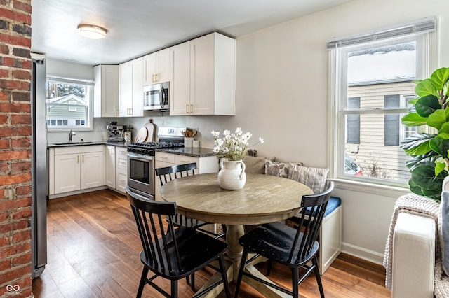 kitchen with sink, stainless steel appliances, white cabinetry, and hardwood / wood-style floors