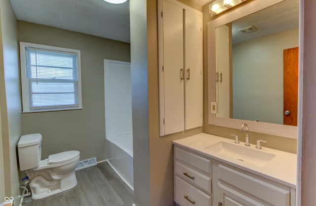 full bathroom featuring a washtub, toilet, wood finished floors, visible vents, and vanity