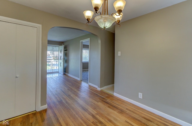 unfurnished dining area featuring arched walkways, a notable chandelier, wood finished floors, and baseboards