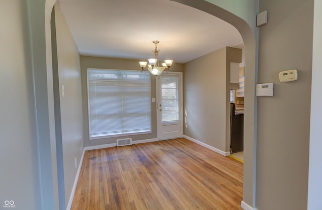 interior space featuring light wood-style floors, visible vents, arched walkways, and baseboards