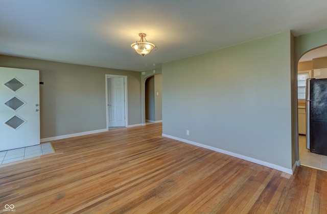 unfurnished room with light wood-type flooring, baseboards, and arched walkways