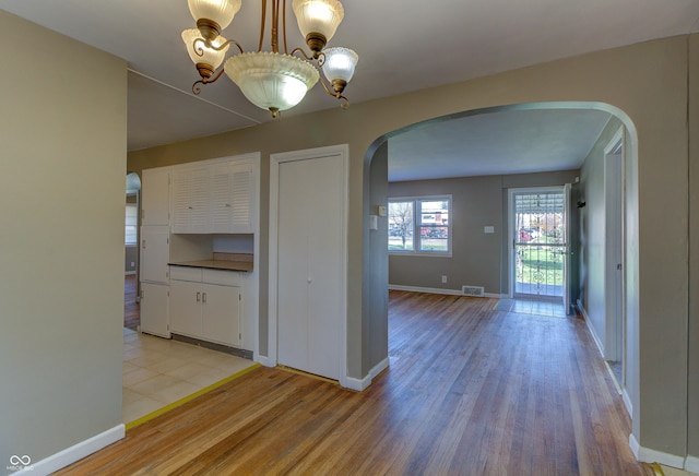 interior space with arched walkways, visible vents, light wood-style flooring, and baseboards