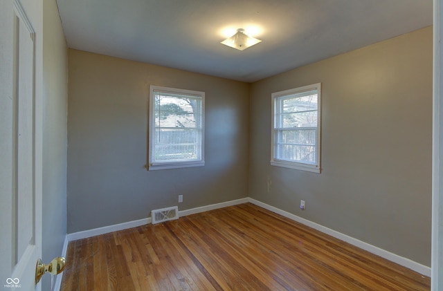 spare room with visible vents, plenty of natural light, baseboards, and wood finished floors