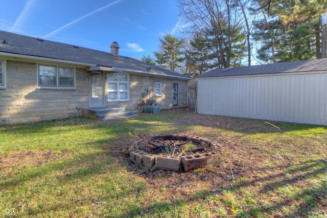 back of property featuring stone siding, a fire pit, and a lawn