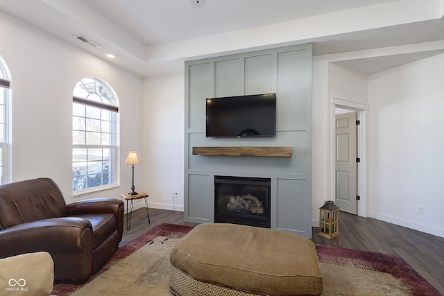 living room featuring visible vents, baseboards, dark wood-type flooring, and a glass covered fireplace