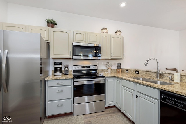 kitchen with light wood-type flooring, light stone counters, recessed lighting, appliances with stainless steel finishes, and a sink