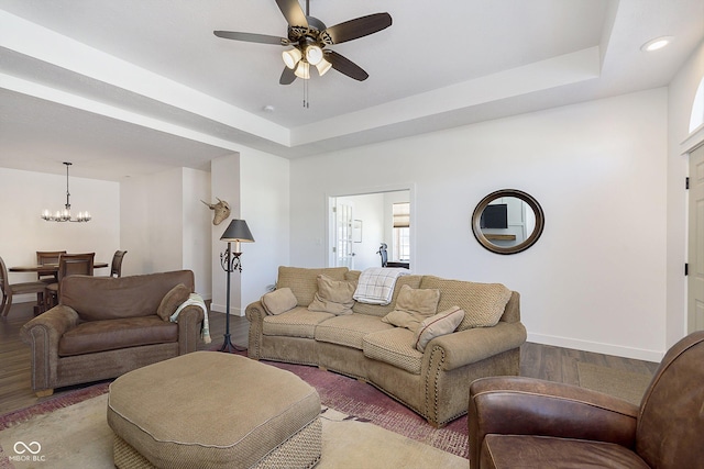 living room featuring ceiling fan with notable chandelier, a tray ceiling, wood finished floors, and baseboards