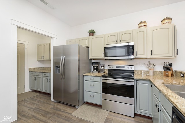 kitchen with light stone counters, stainless steel appliances, dark wood-type flooring, and visible vents