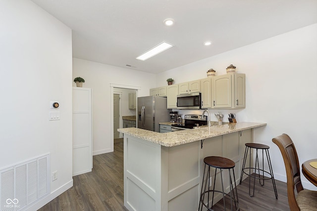 kitchen featuring visible vents, a breakfast bar, a peninsula, dark wood-style flooring, and stainless steel appliances