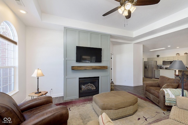 living area with a glass covered fireplace, a raised ceiling, wood finished floors, and baseboards