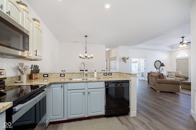 kitchen with light stone counters, dark wood finished floors, a peninsula, a sink, and stainless steel appliances