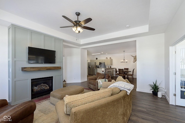 living area with a fireplace, a ceiling fan, dark wood-type flooring, and a tray ceiling