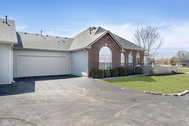 view of front facade featuring aphalt driveway, fence, roof with shingles, a front yard, and brick siding