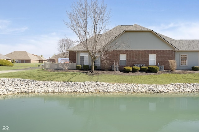 rear view of house with fence, a yard, central AC, a water view, and brick siding