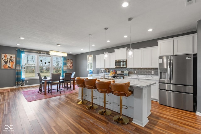 kitchen featuring white cabinetry, pendant lighting, stainless steel appliances, a kitchen island with sink, and backsplash