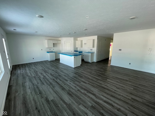 kitchen with a textured ceiling, dark hardwood / wood-style flooring, white cabinetry, and a kitchen island