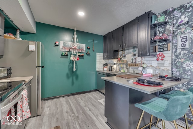 kitchen with a textured ceiling, light hardwood / wood-style floors, tasteful backsplash, kitchen peninsula, and a breakfast bar area