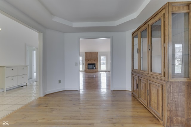 corridor with light wood finished floors, baseboards, and a tray ceiling