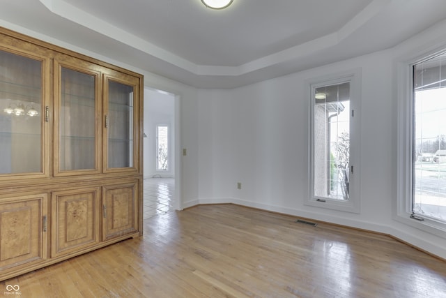 spare room featuring visible vents, baseboards, a raised ceiling, and light wood-style floors