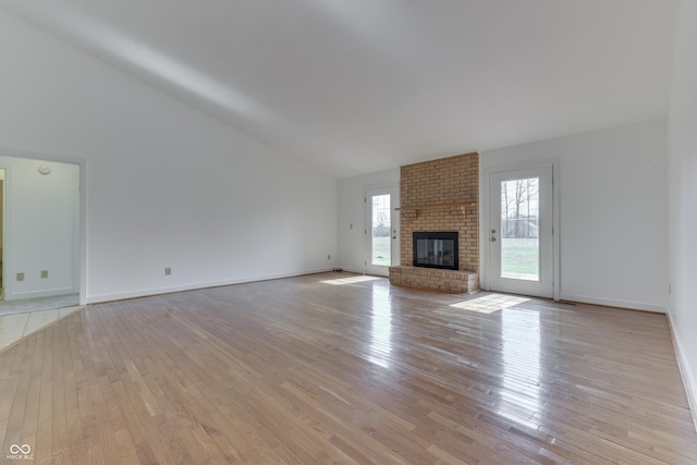 unfurnished living room with a fireplace, high vaulted ceiling, light wood-type flooring, and baseboards