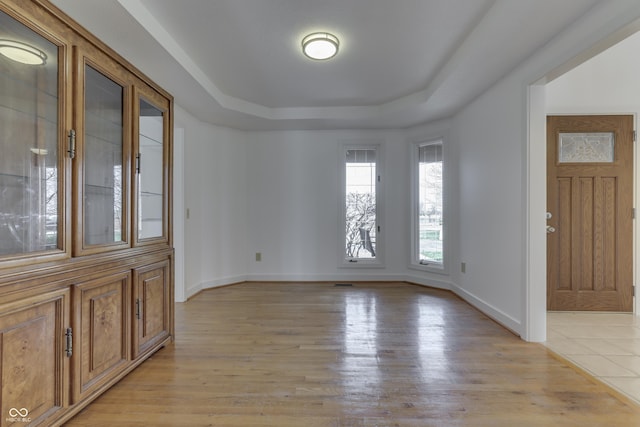 entrance foyer featuring a tray ceiling, light wood-type flooring, and baseboards