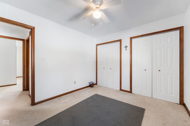 unfurnished bedroom with ceiling fan, light colored carpet, and multiple closets