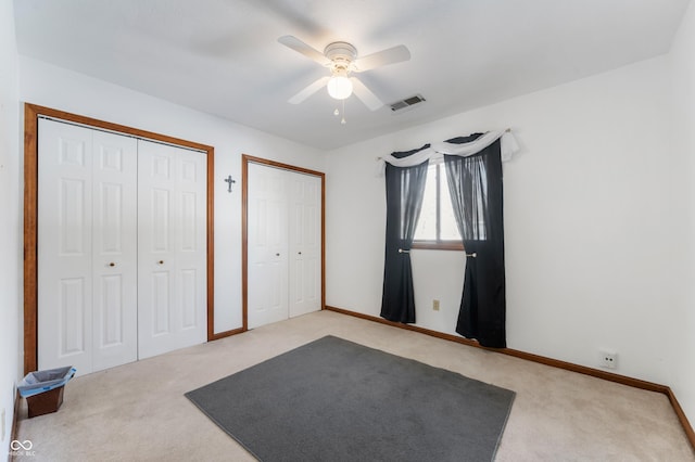 unfurnished bedroom with ceiling fan, light colored carpet, and multiple closets