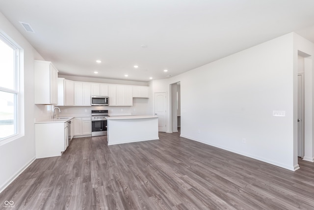 kitchen with sink, white cabinets, wood-type flooring, a kitchen island, and appliances with stainless steel finishes