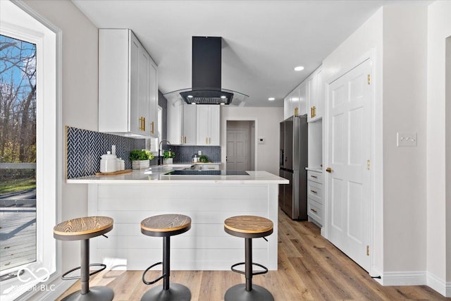 kitchen with kitchen peninsula, white cabinets, island exhaust hood, and a kitchen bar