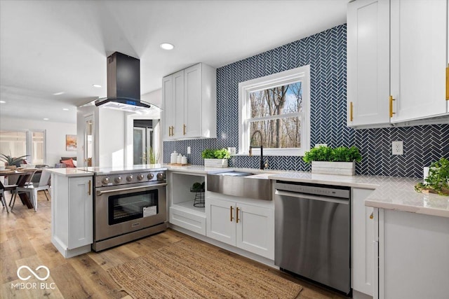 kitchen with island range hood, appliances with stainless steel finishes, light wood-type flooring, white cabinets, and sink