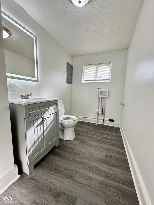 bathroom featuring a textured ceiling, electric panel, hardwood / wood-style floors, toilet, and vanity