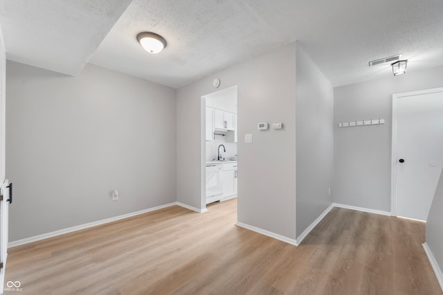 hall featuring a textured ceiling, light wood-type flooring, and sink