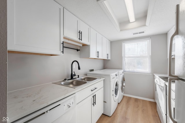 clothes washing area featuring sink, light hardwood / wood-style flooring, washing machine and dryer, and a textured ceiling