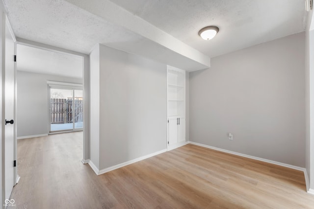 interior space with built in shelves, a textured ceiling, and light wood-type flooring