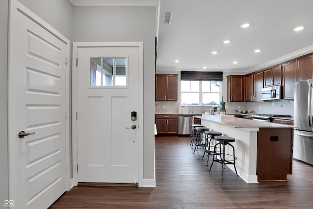 kitchen featuring appliances with stainless steel finishes, a center island, dark wood-type flooring, tasteful backsplash, and a breakfast bar