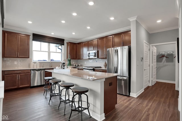 kitchen featuring a kitchen island, stainless steel appliances, light stone counters, crown molding, and a breakfast bar area