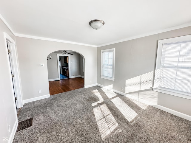 empty room with ornamental molding, ceiling fan, and dark colored carpet