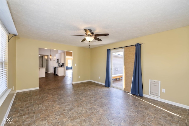 empty room featuring ceiling fan with notable chandelier and a textured ceiling