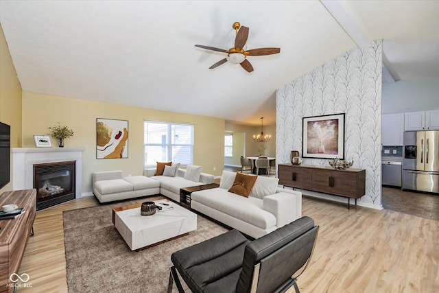 living room with ceiling fan with notable chandelier, light hardwood / wood-style floors, and vaulted ceiling