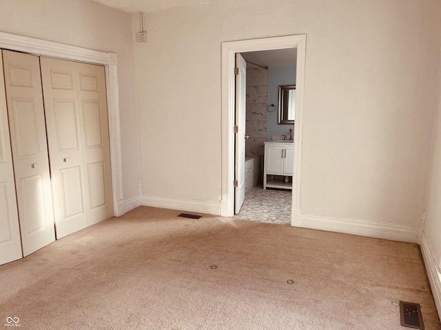 unfurnished bedroom with connected bathroom, sink, light colored carpet, and a closet