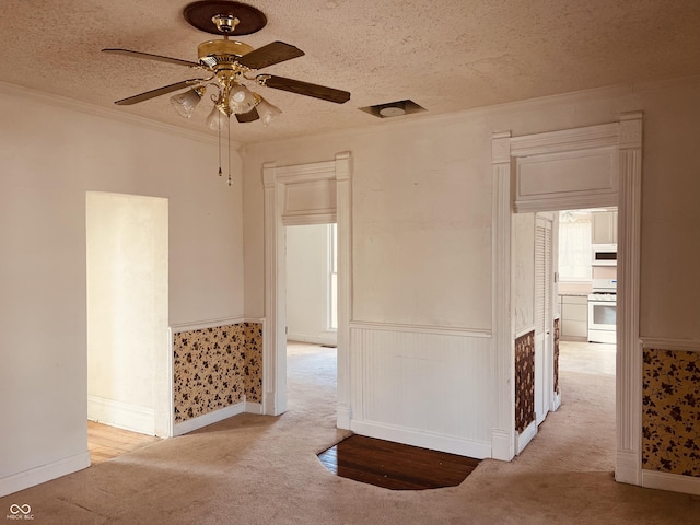 carpeted empty room with ceiling fan, crown molding, and a textured ceiling